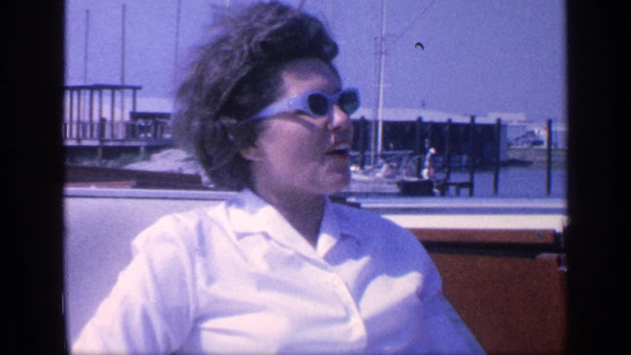 The woman turns to the side in a wooden boat, with docks, masts, and Florida water visible in the 1968 home-movie frame.