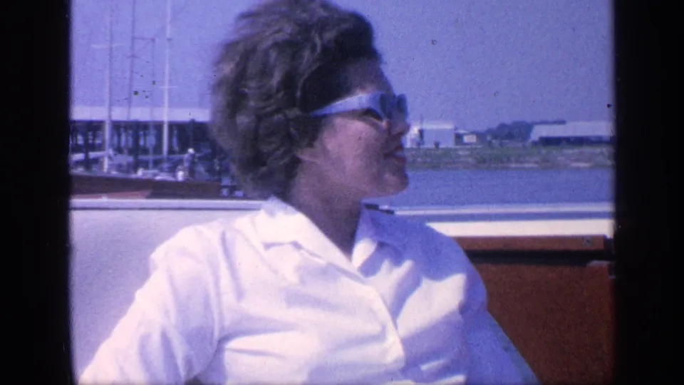 The woman turns her head in profile while seated in the boat, her hair blown by wind against a Florida marina backdrop.