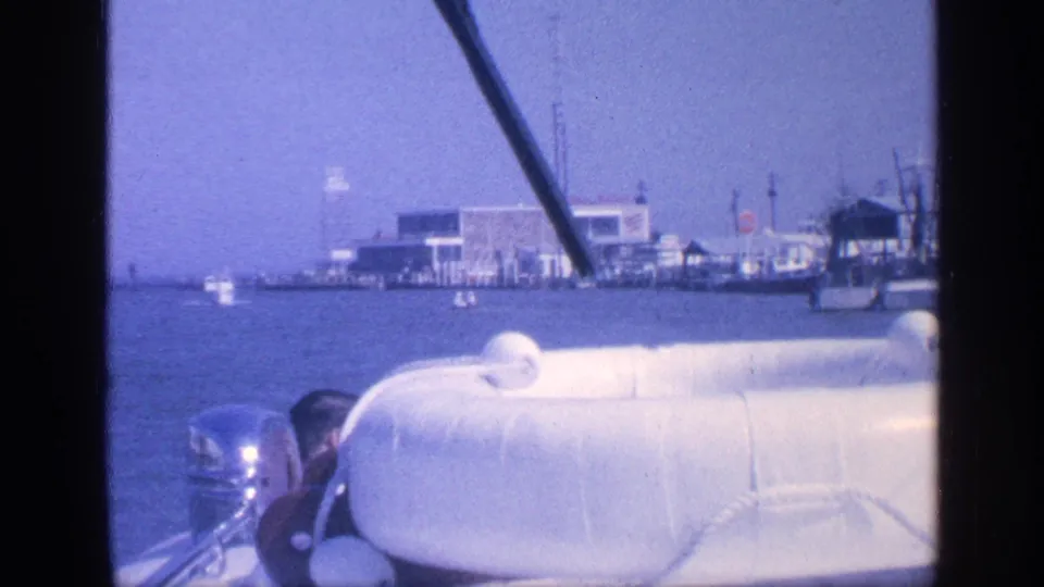 1968 Florida boating footage with a white seat in the foreground and a low waterfront with docks and vessels in the distance.