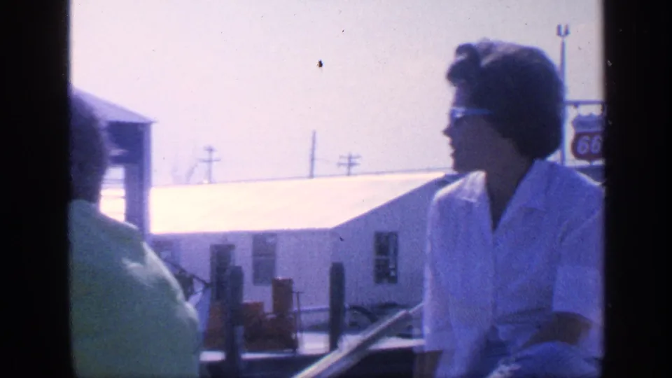In the 1968 Florida home-movie clip, a woman in a white blouse and sunglasses sits on a boat near waterfront buildings.