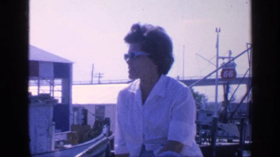 A woman in sunglasses sits on a boat in supplied 1968 Florida footage, with shoreline structures and a 66 shield-style sign visible.