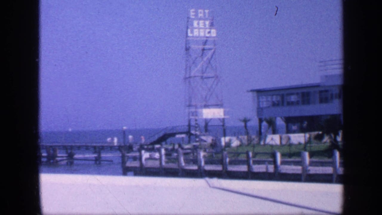 Florida beach pier scene with Eat Key Largo tower sign, stilted building, railings, and ocean horizon.