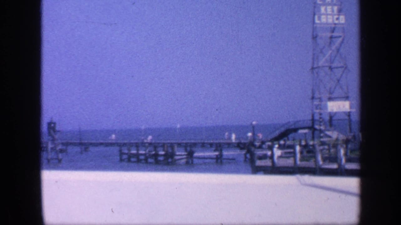 1968 Florida coastal frame showing pier railings, ocean horizon, beach promenade, and a partially visible Eat Key Largo tower sign.