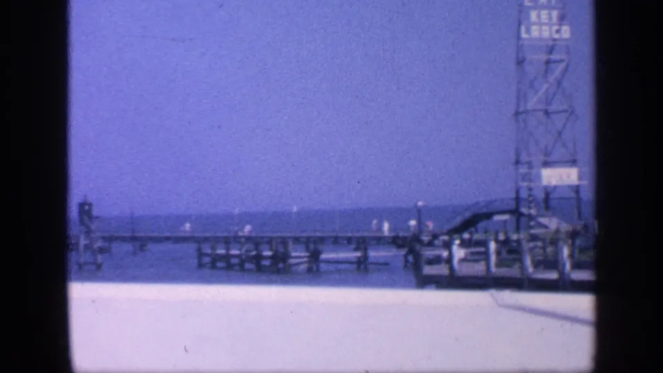 1968 Florida coastal frame showing pier railings, ocean horizon, beach promenade, and a partially visible Eat Key Largo tower sign.