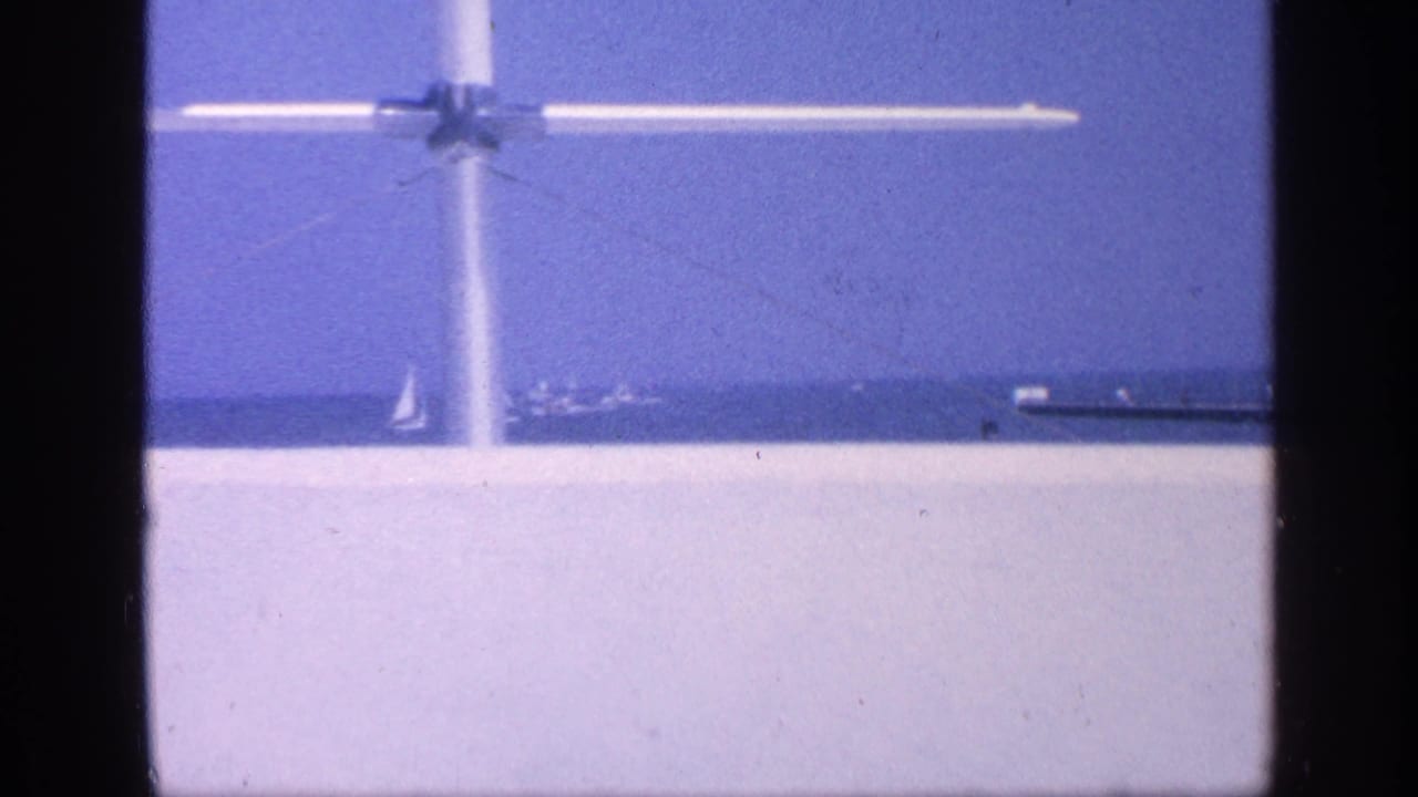 White aircraft passes above open water with a distant structure near the horizon.