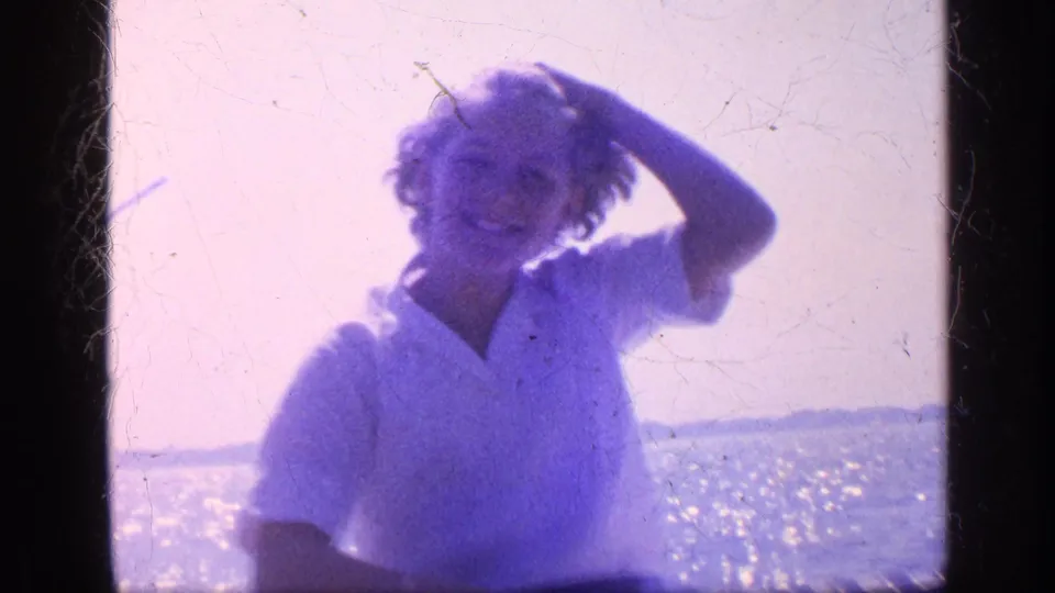 1968 Florida 8mm frame of a smiling young woman on a boat pushing back her hair in the sea breeze.
