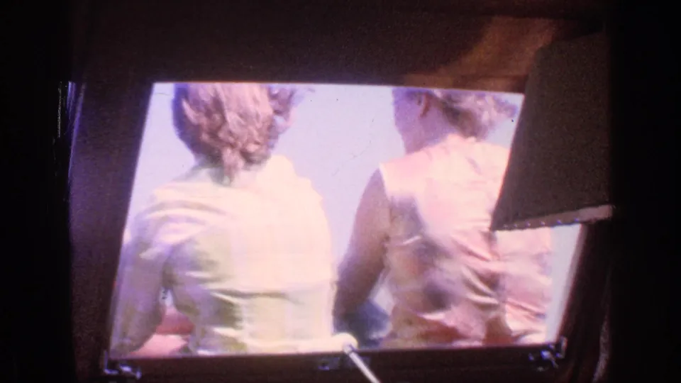 The final frame shows two adults from behind in a sunlit travel setting, with dark structural edges and 8mm film texture.