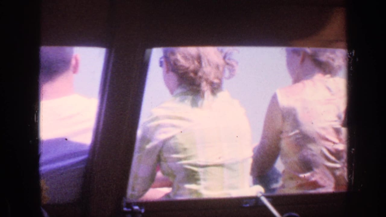 Passengers seen from behind inside a boat, including a woman in a light top and another person in a sleeveless shirt.