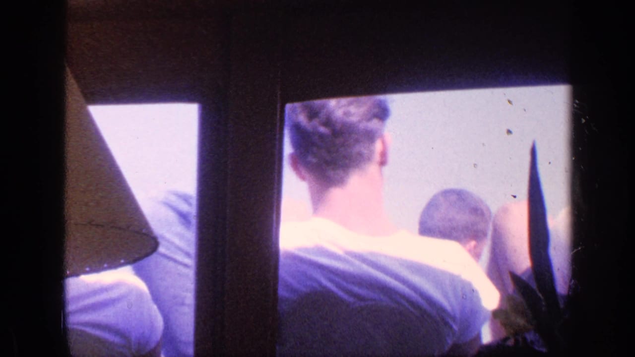 Young men seen from behind through window panes, with a lampshade at the left edge.