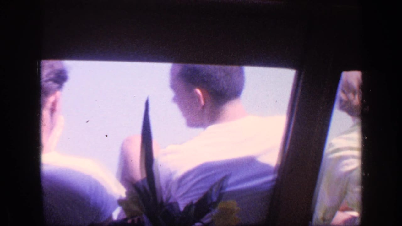 1968 Florida home-movie still showing passengers from behind inside a windowed transport setting, with overexposed water or sky beyond.