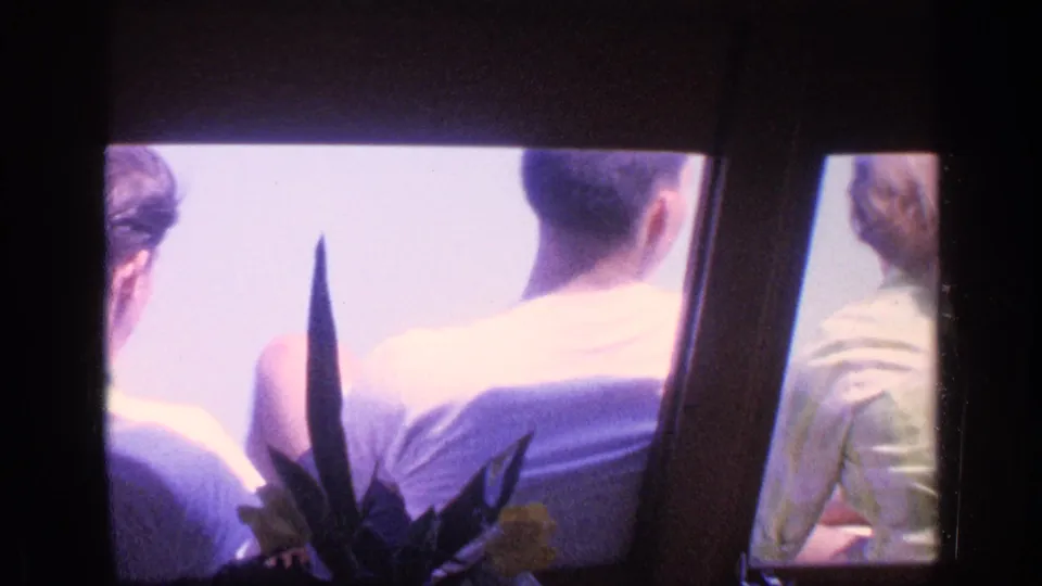 1968 Florida 8mm still of passengers seated by windows, including a man in a light shirt and a foreground plant silhouette.