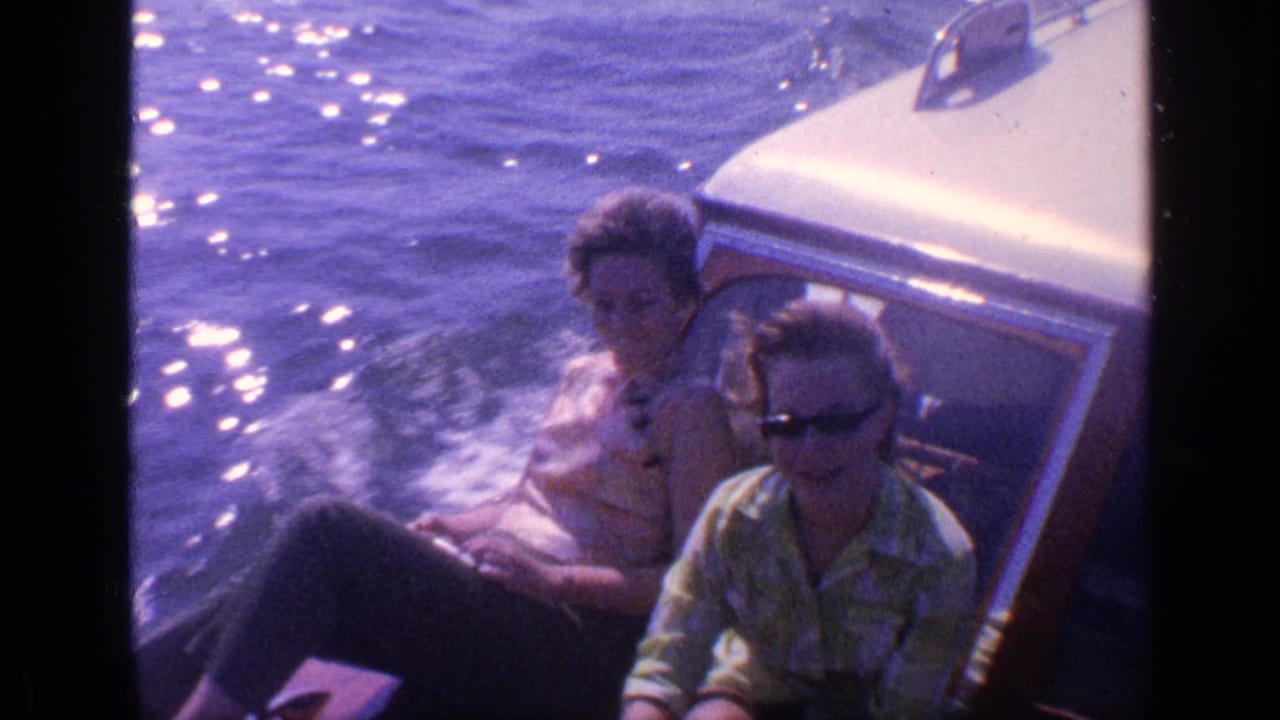 Two adults sit beside a boat cabin as sunlight sparkles on the water.