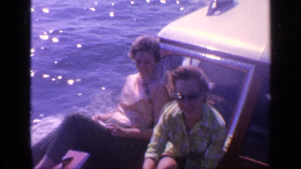 1968 Florida home-movie frame showing adults seated on a motorboat, with glare on the water and soft 8mm color.