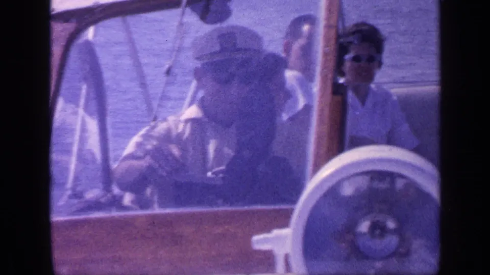 Aged 8mm frame from a 1968 Florida boat outing, with a driver at the helm and a woman in sunglasses visible behind him.