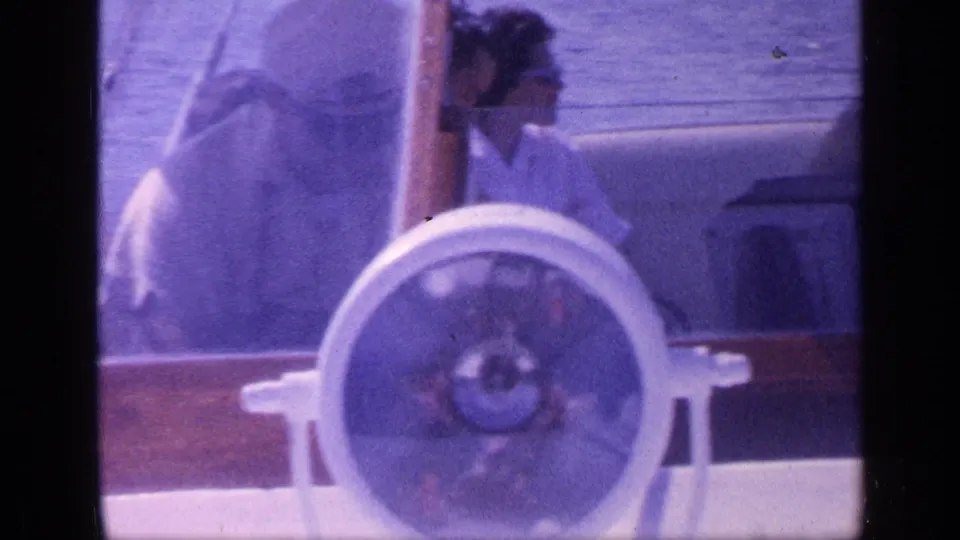 1968 Florida home-movie frame with seated passengers partly obscured by the windshield and large white wheel on a motorboat.
