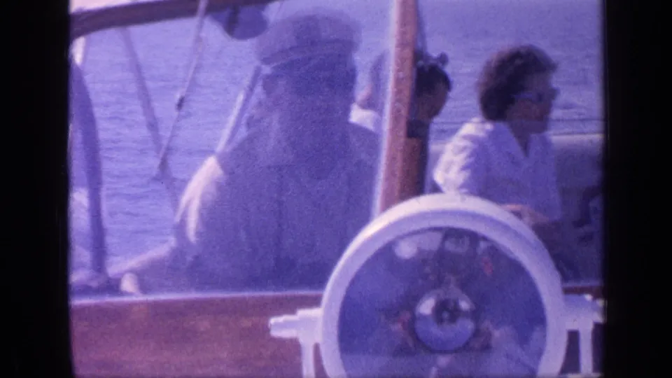 1968 Florida home-movie frame of several passengers around the helm area of a wooden-trimmed motorboat on calm water.
