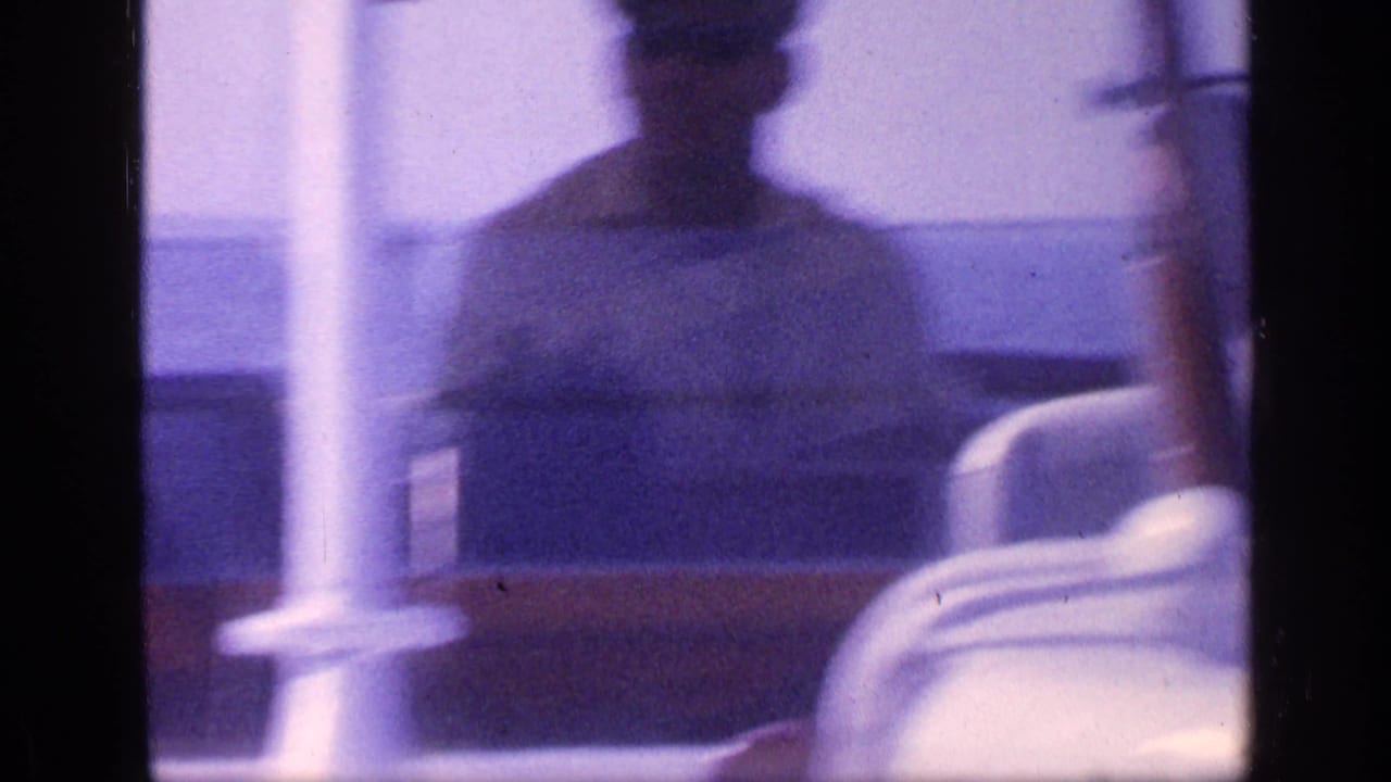 Blurred adult figure seen through boat structure with calm water behind.