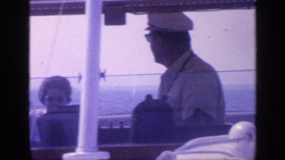 1968 Florida 8mm frame showing a man in a captain-style hat at the helm while a woman sits nearby on a boat deck.