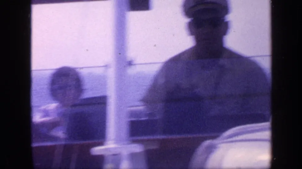 Florida 1968 home-movie frame showing a man in a captain-style hat and sunglasses near the helm with a woman seated behind him.