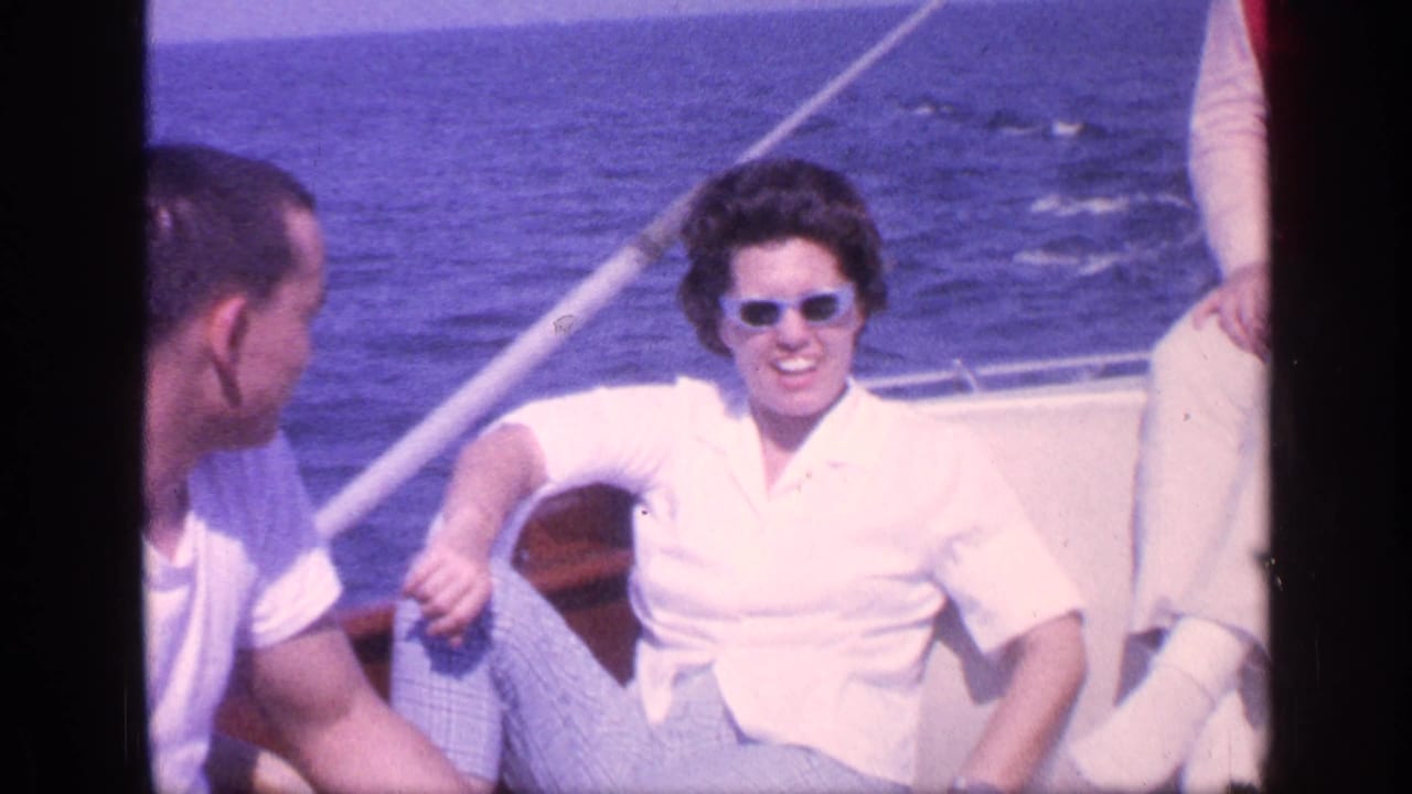 1968 Florida home-movie frame of a man in a white shirt facing a woman in sunglasses on a boat, with open water behind them.