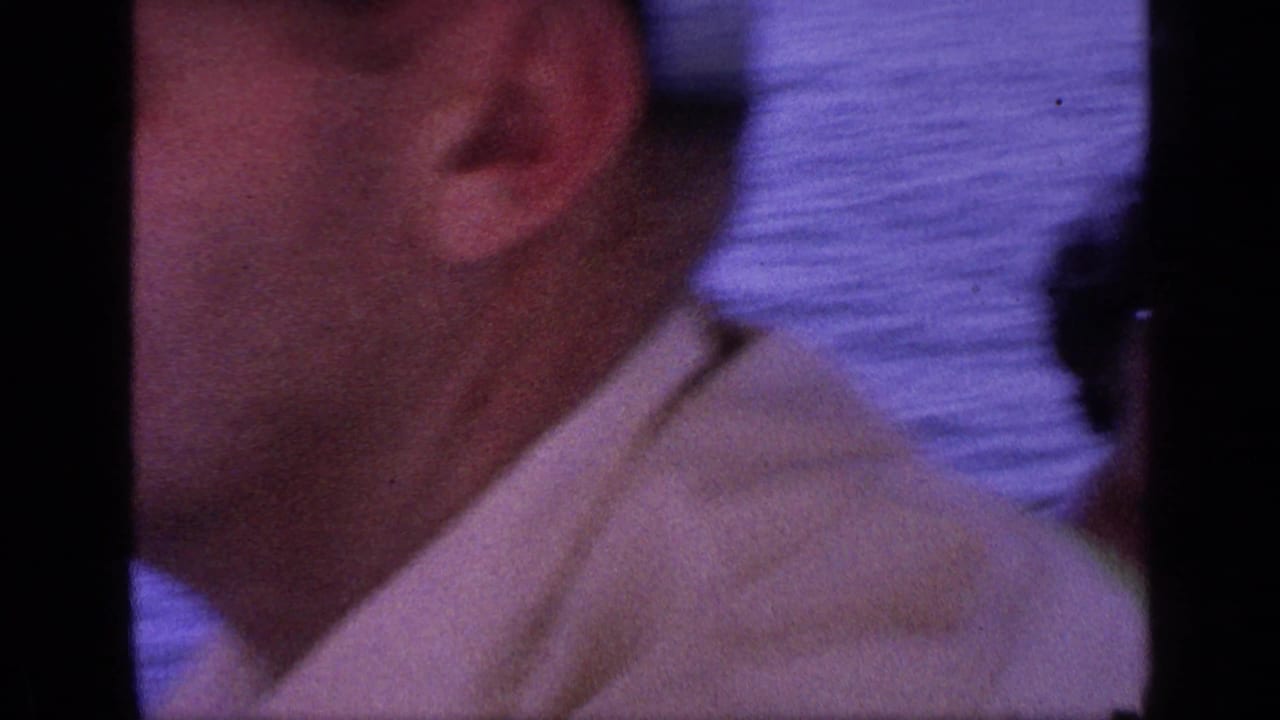 Soft close-up of a man's face and white shirt with blue water behind him.