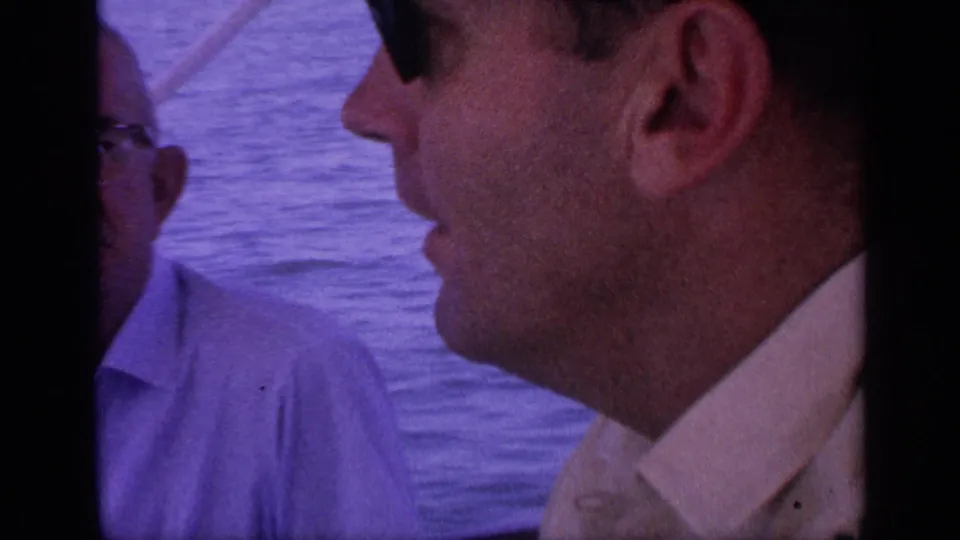 1968 Florida boating footage showing a man's side profile in a light shirt, with another adult partly framed against the water.