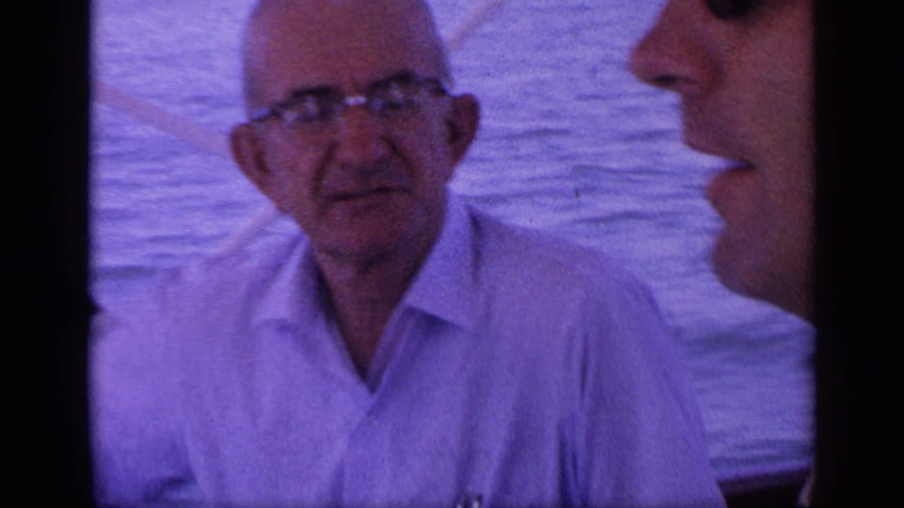 Older man in glasses faces the camera aboard a boat with water behind him.