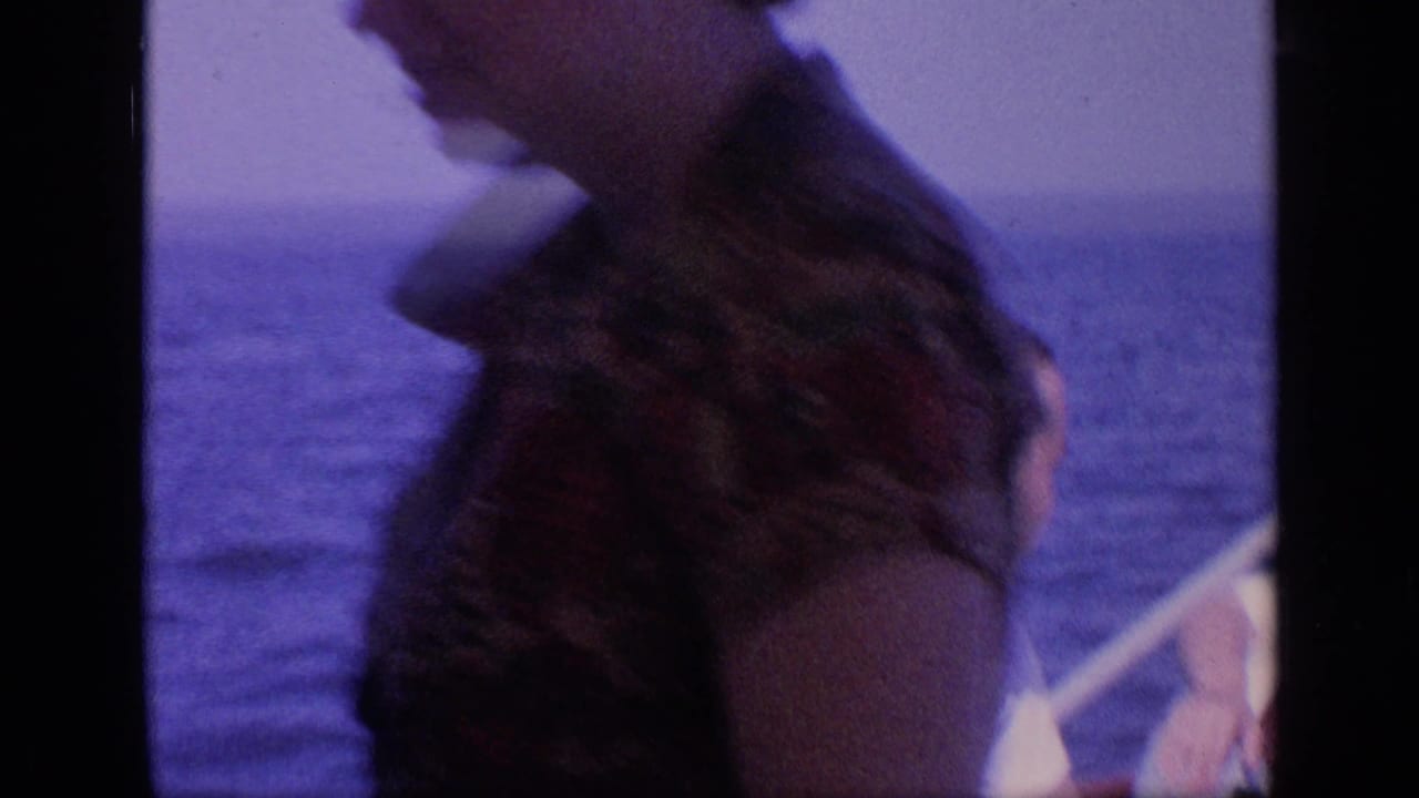 Woman seated on a boat near the sea, partly blurred by motion and film softness.