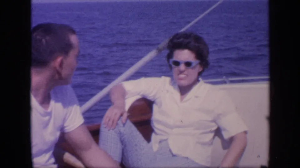 1968 Florida 8mm frame showing two adults seated on a boat, including a sunglasses-wearing person in a white shirt, with sea and railing behind them.