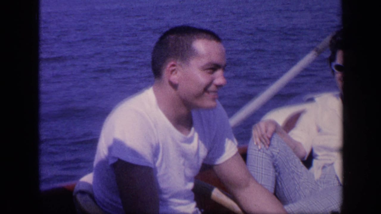 Smiling young man on a boat beside a companion wearing sunglasses.