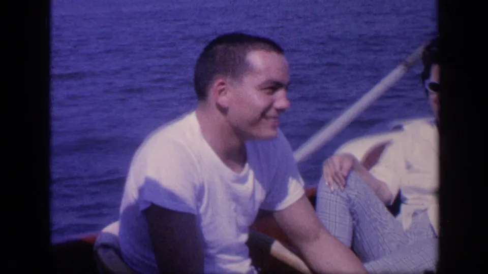 A smiling young man sits beside a woman in sunglasses on a Florida boat trip, with open water and a pale rail behind them.