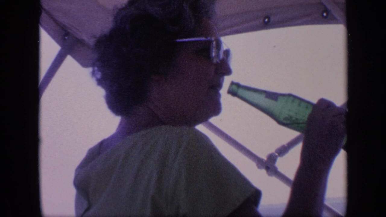 Woman in sunglasses holds a green glass bottle near her mouth under a boat canopy.