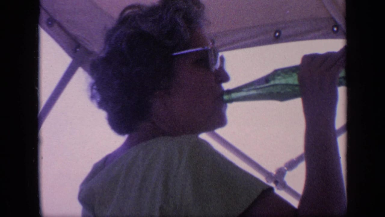Woman in sunglasses drinks from a green glass bottle while seated beneath a canopy.