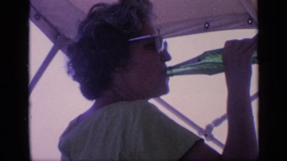The woman drinks from a green glass bottle on a boat, with canopy fabric and metal supports visible behind her in 1968 Florida footage.