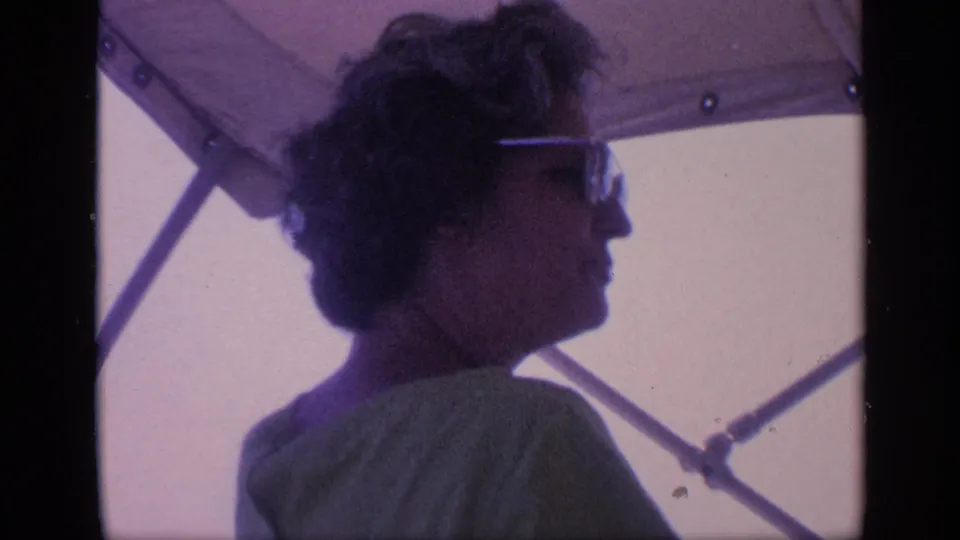 A woman in sunglasses sits in profile on a boat in Florida, looking aside beneath canopy supports after drinking from a bottle.