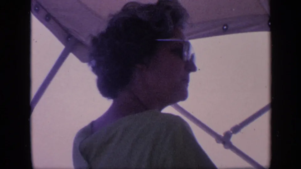 The clip ends with the woman seated in profile under the boat canopy, her sunglasses and light shirt visible in soft 8mm color.