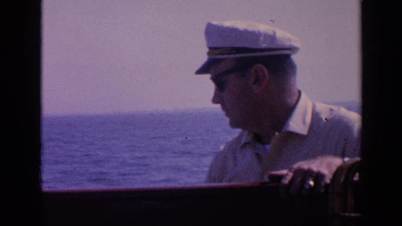 Adult man in a white captain's hat and sunglasses leans near a boat railing during a 1968 Florida boating scene, with ocean visible behind him.