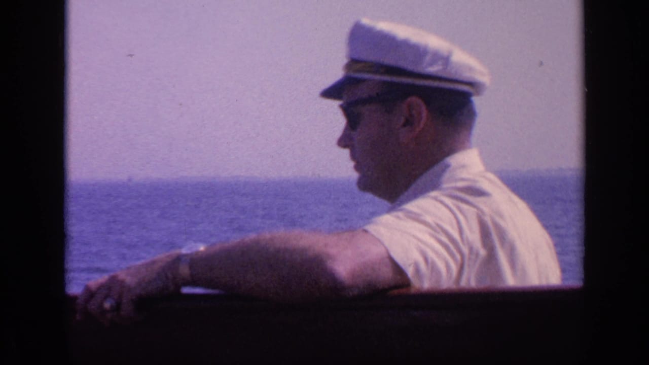 Profile view of a man in a white cap and sunglasses leaning on a boat rail above the sea.