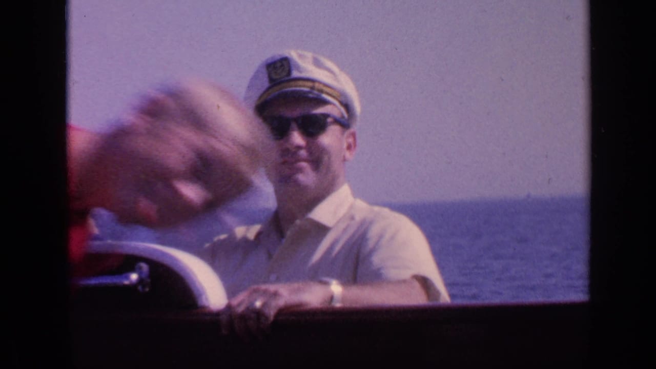 Man at the boat wheel partly obscured by a blurred foreground person.
