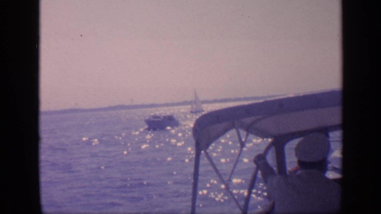 1968 Florida boating view across sunlit water, with a nearby vessel and a distant sailboat visible near the horizon.
