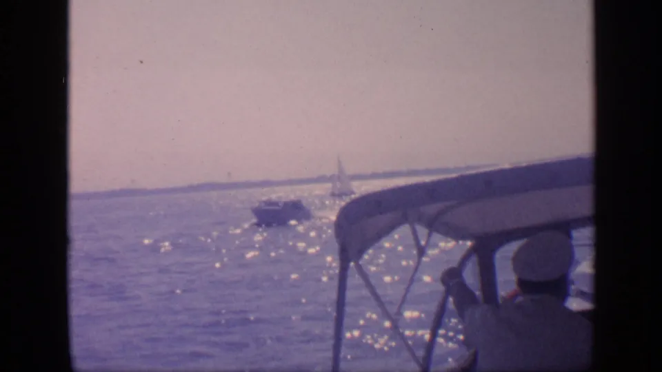 1968 Florida boating view across sunlit water, with a nearby vessel and a distant sailboat visible near the horizon.