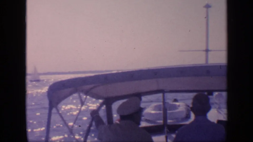 1968 Florida boating frame with people under a canopy, sunlit water behind them, and a sailboat faintly visible near the horizon.