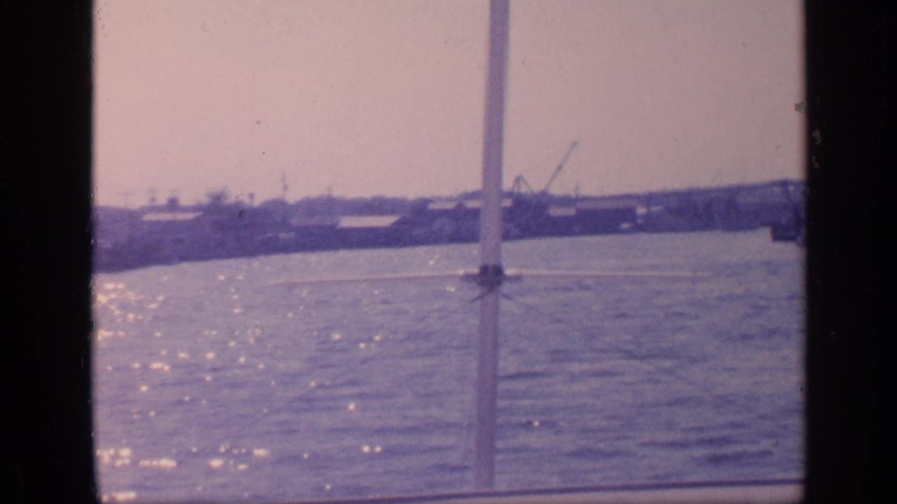 Boat-framed view across water toward a distant bridge and port shoreline.