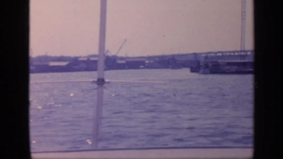 1968 Florida boat view with dark vertical framing, open water, a bridge span, and distant industrial shoreline structures.
