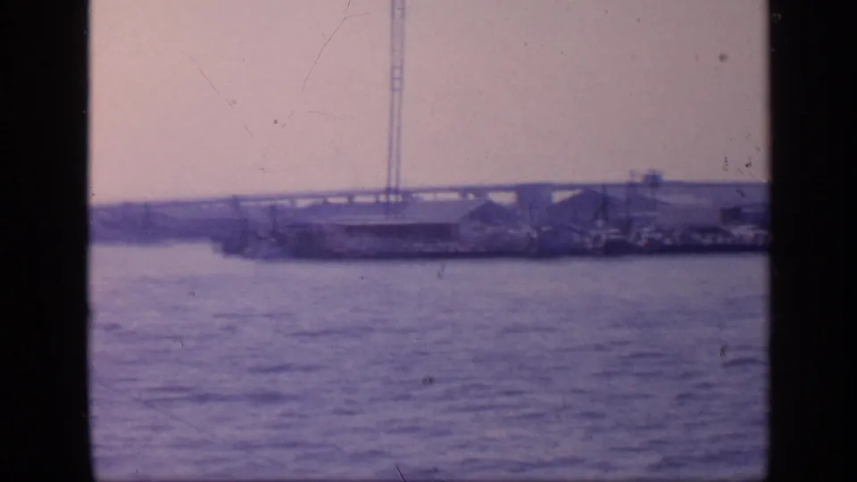 1968 Florida boat-shot frame with blue-tinted water, distant bridge spans, waterfront buildings, and vertical foreground framing.