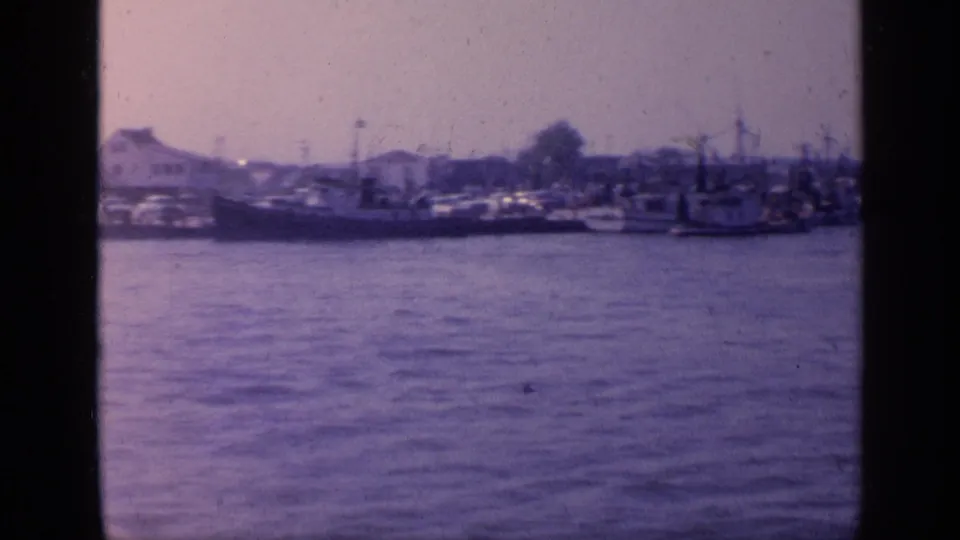 1968 Florida 8mm harbor frame with fishing boats, low shoreline buildings, and rippled water.