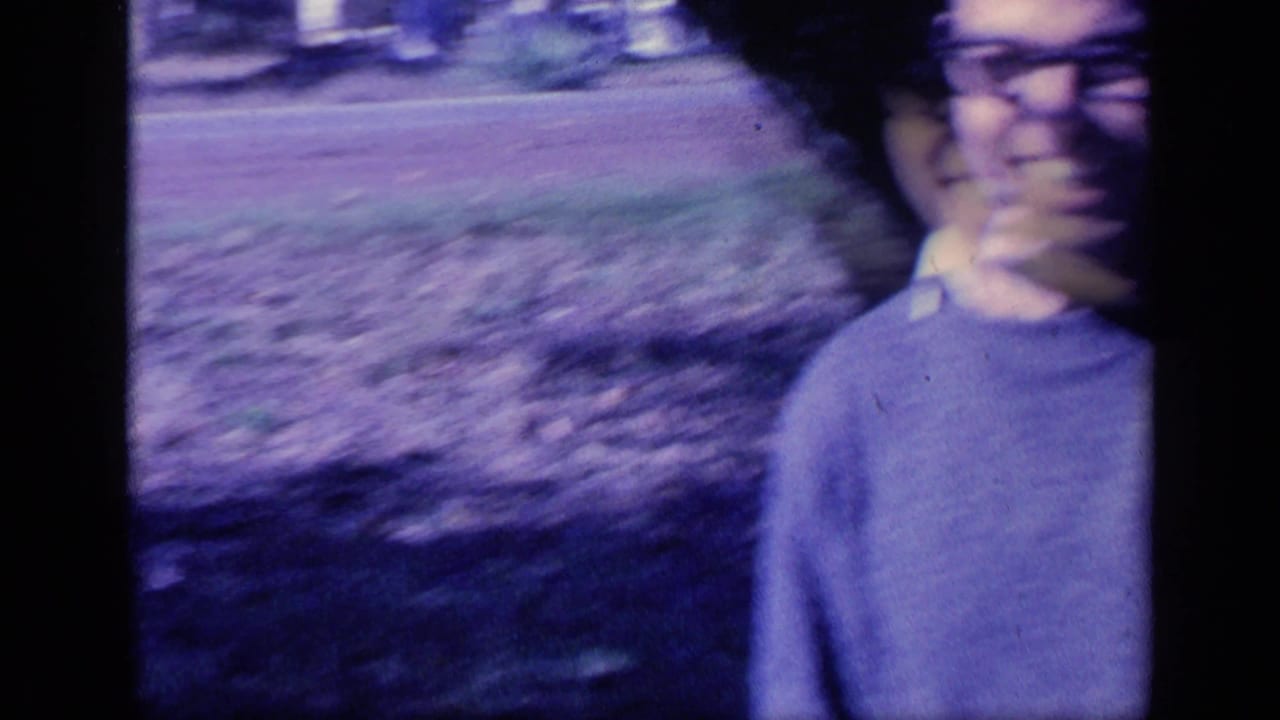 Young man wearing glasses smiles near a grassy area in handheld 1968 Florida 8mm footage.