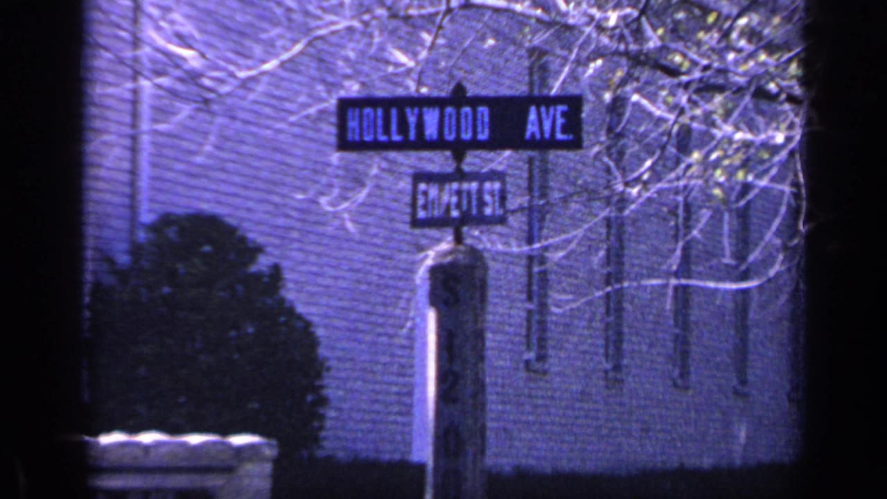 1968 Florida 8mm frame with Hollywood Ave and Em/ett St signs, a signpost, brick exterior, shrubbery, and bare tree limbs.