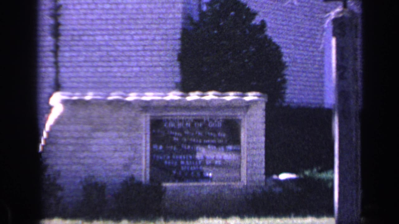 1968 Florida 8mm frame showing a stone church sign outside a brick church building with shrubs and grass.
