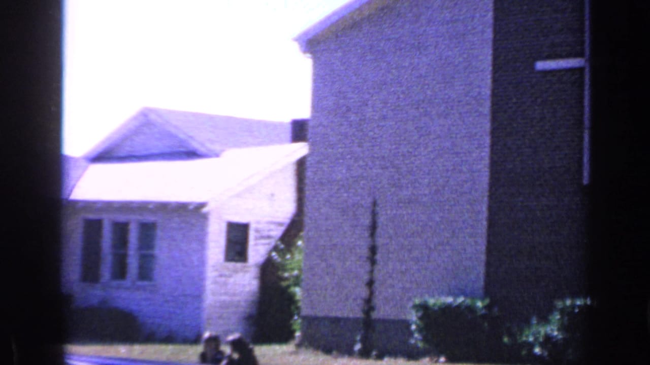 Florida church exterior seen from a residential angle, with pale walls, windows, lawn, and part of a larger brick structure.